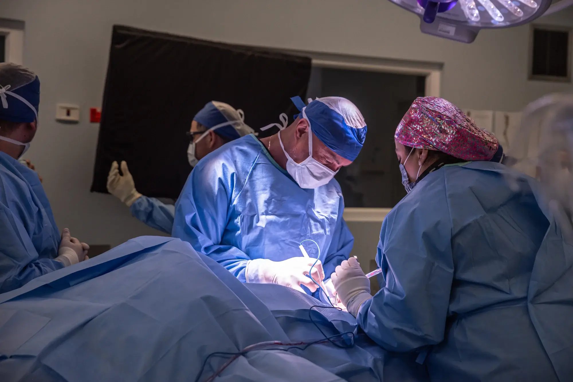 Equipo médico realizando cirugía en un quirófano con indumentaria estéril azul.