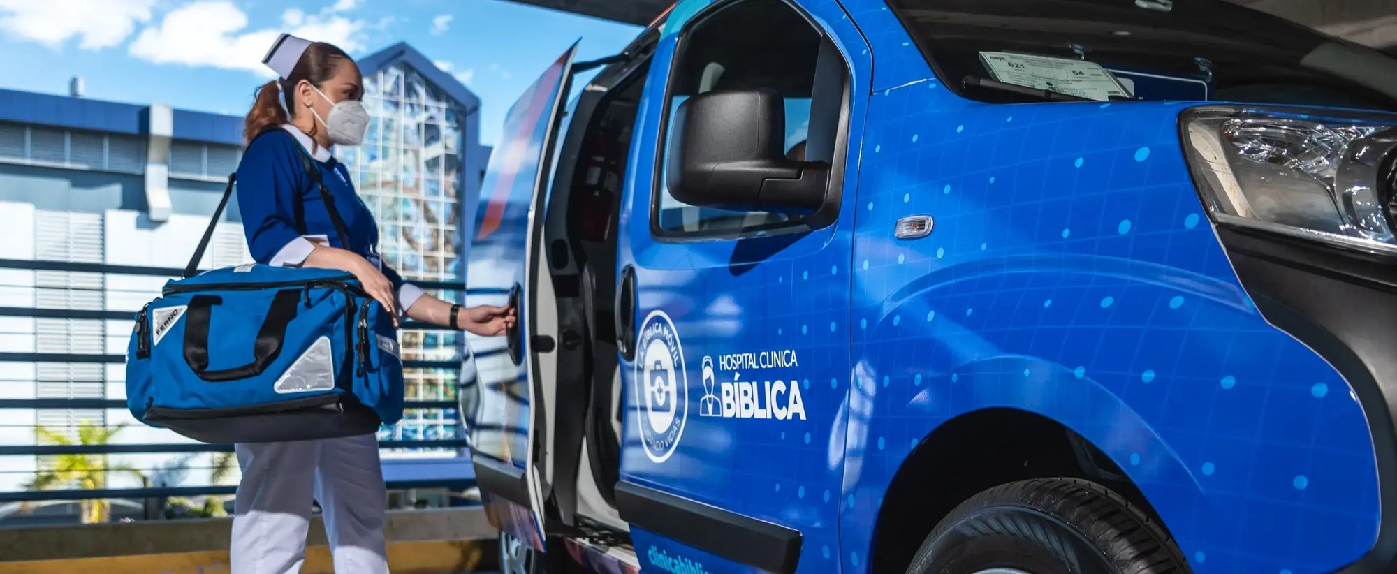 Enfermera de la Clínica Bíblica abre la puerta de una unidad de la Bíblica Móvil, con uniforme azul y un bolso médico.