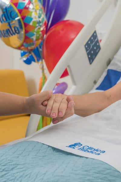 Mano de una persona sosteniendo la mano de una paciente acostada en una cama de hospital. Mano de una persona sosteniendo la mano de una paciente acostada en una cama de hospital.