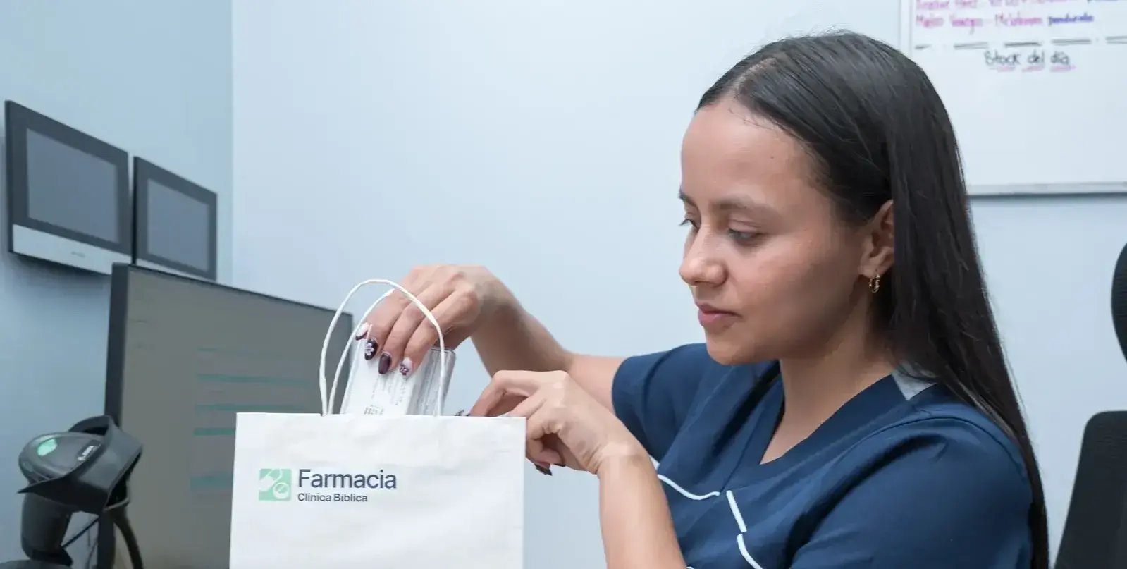 Empleada de farmacia de la Clínica Bíblica coloca medicamentos dentro de una bolsa blanca con el logo de Farmacia Clínica Bíblica.