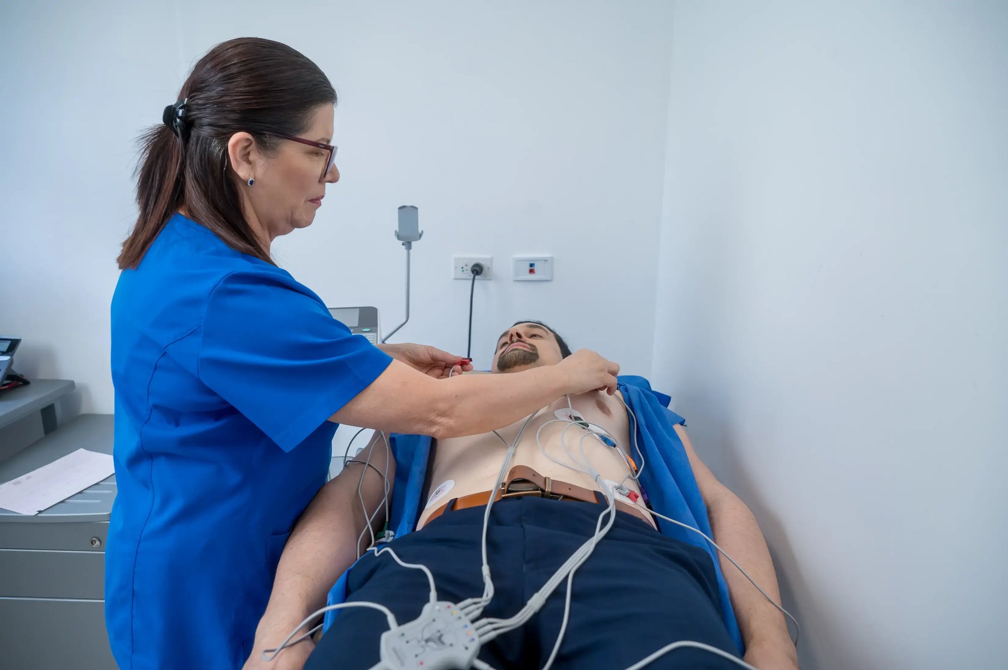 Profesional de salud colocando electrodos en el pecho de un paciente recostado para realizar un electrocardiograma.