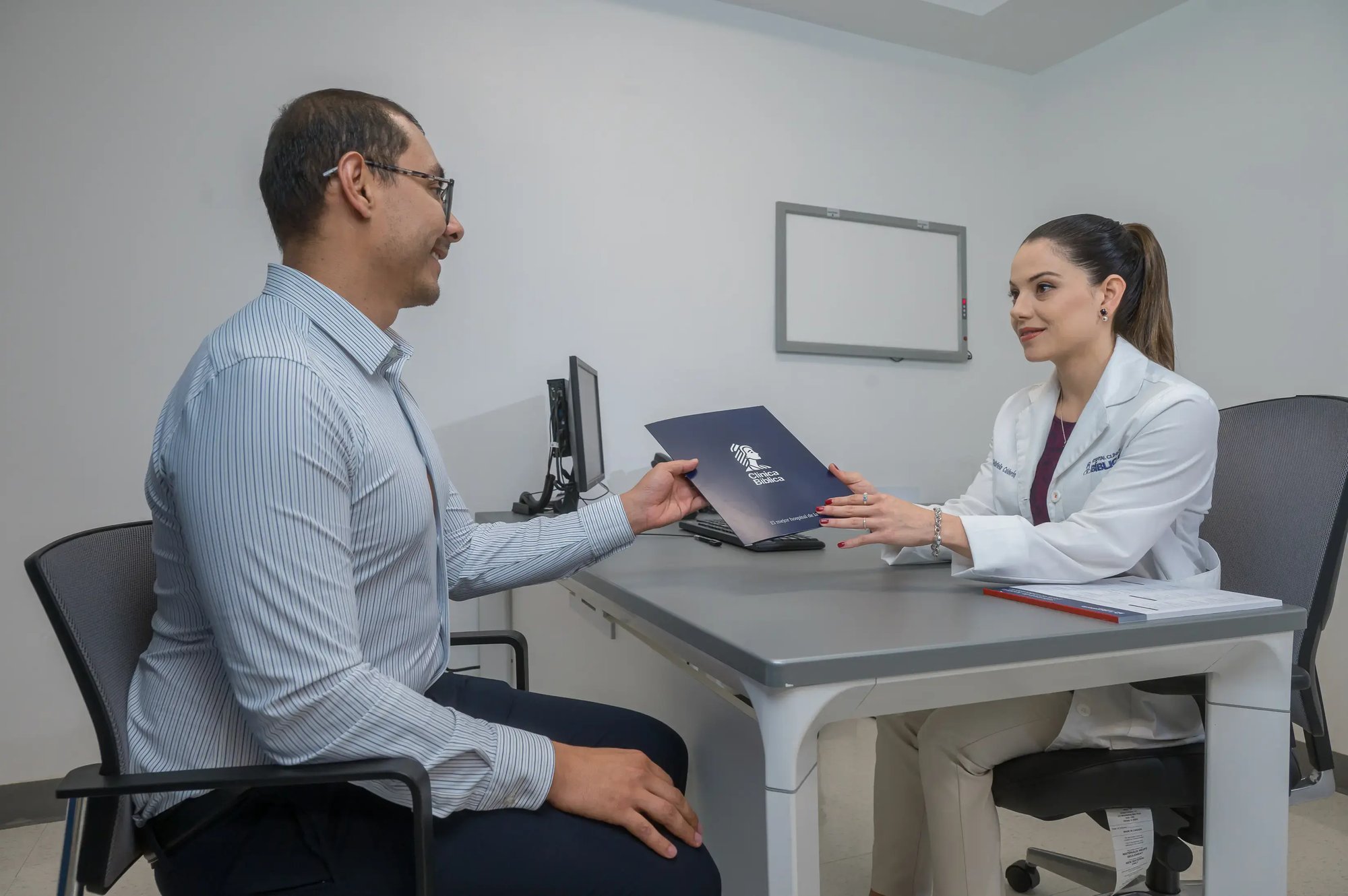 Médico entregando un documento informativo a un paciente durante una consulta en un consultorio clínico. Médico entregando un documento informativo a un paciente durante una consulta en un consultorio clínico.
