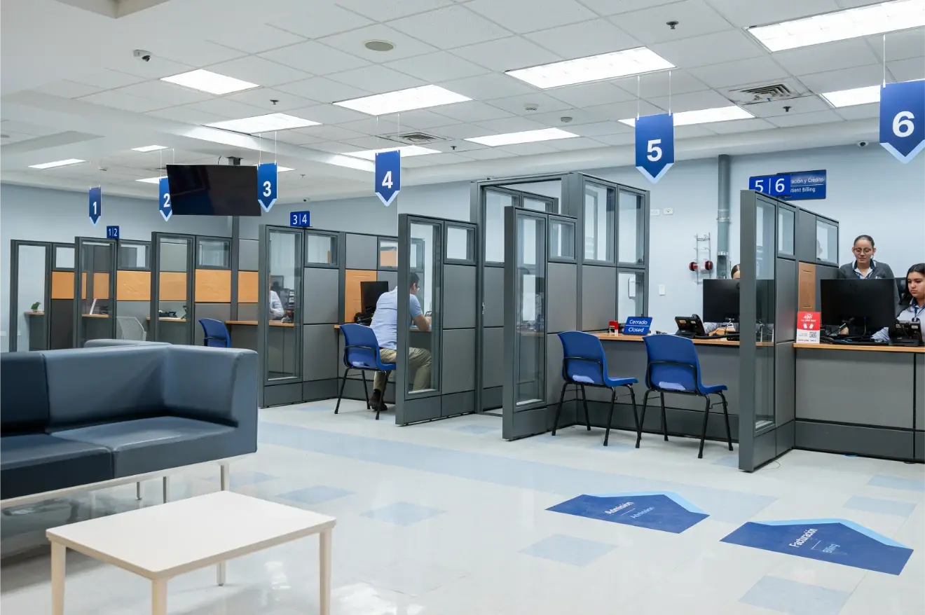 Clínica Bíblica's customer service area with numbered modules, blue chairs and staff in their cubicles.