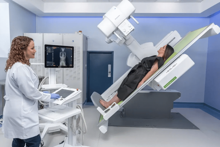 Radiological technique performing an examination of a patient lying on an inclined X-ray table.