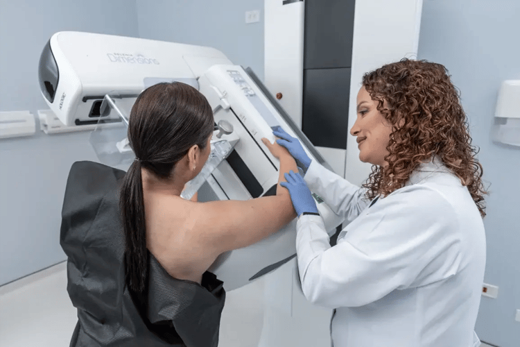 Health technician performing mammography on patient in specialized equipment