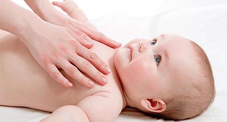 Masaje suave en el pecho de un bebé acostado sobre una superficie blanca.