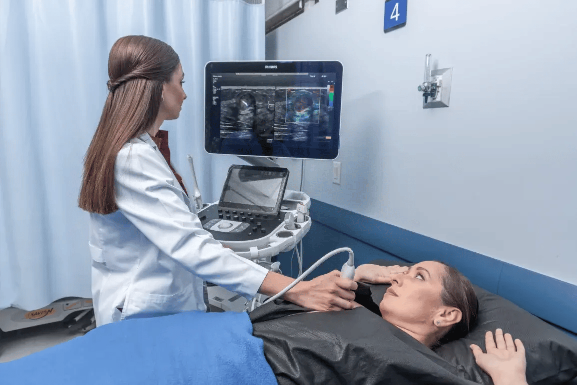 Médica realizando ultrasonido mamario a paciente acostada