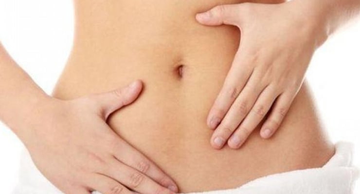 Abdomen femenino con manos apoyadas sobre el vientre bajo, enfocado en la zona abdominal.