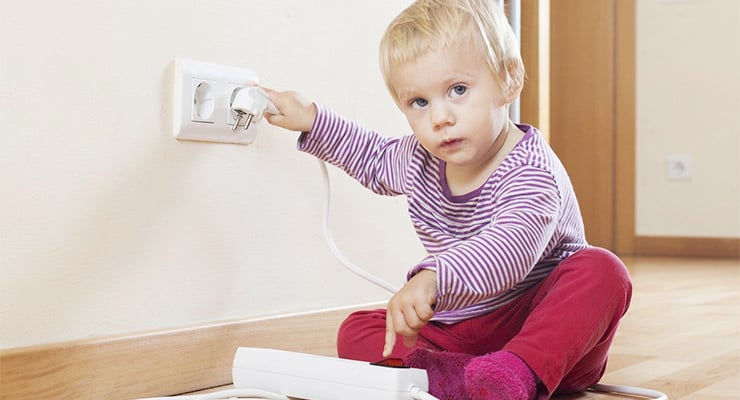 Niño pequeño sentado en el piso manipulando un enchufe eléctrico en la pared