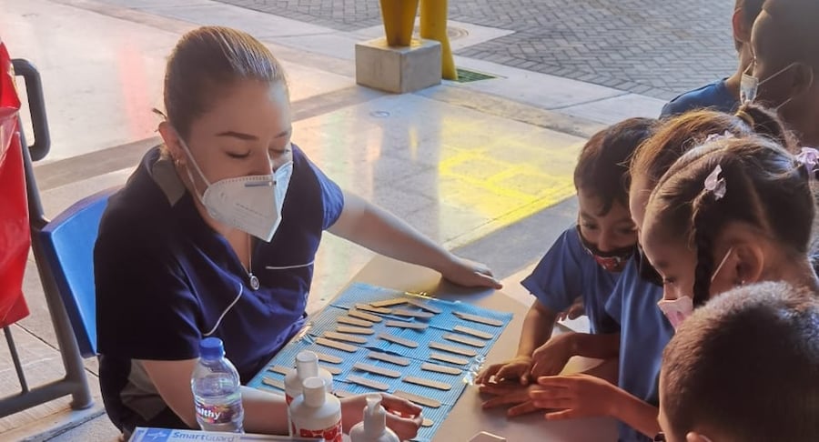 Profesional del Hospital Clínica Bíblica guía actividad lúdica sobre higiene bucal con niños en espacio educativo.