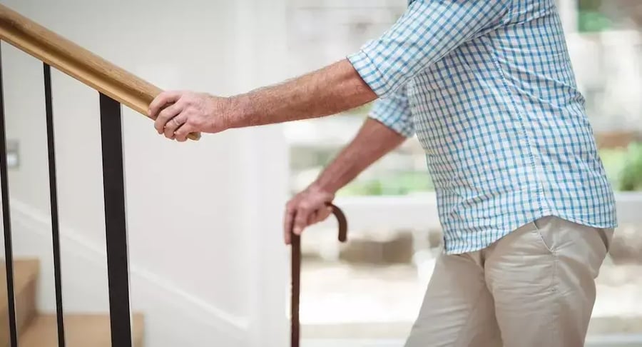Adulto mayor subiendo escaleras con bastón y apoyo en pasamanos