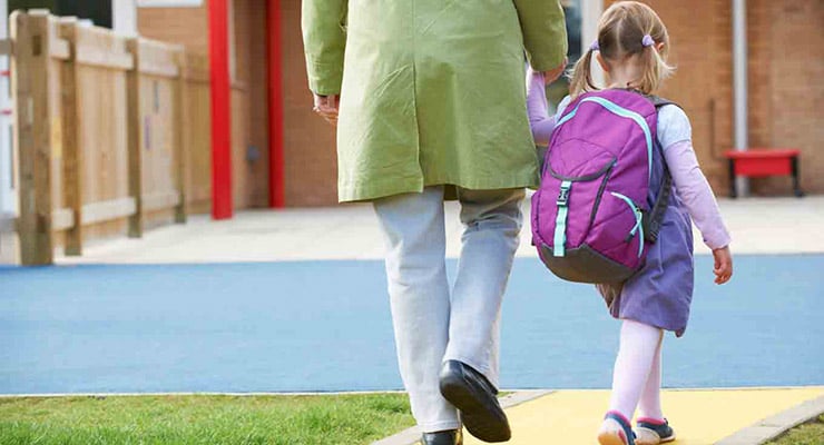 Adulto acompañando a una niña con mochila mientras caminan hacia un centro educativo