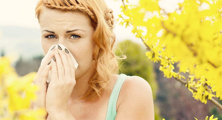 Mujer al aire libre cubriéndose la nariz con un pañuelo entre plantas amarillas.