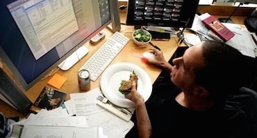 Persona comiendo ensalada frente a una computadora en espacio de trabajo