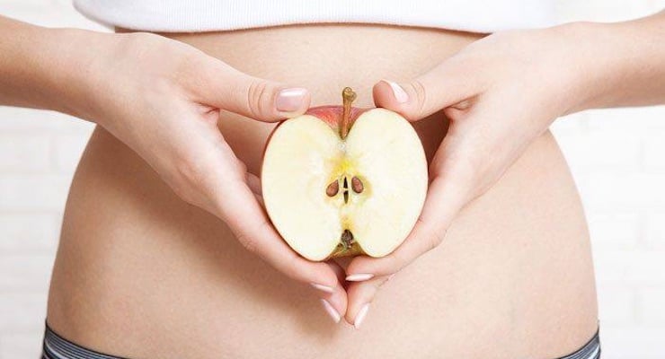 Mujer sosteniendo una manzana cortada a la mitad frente a su vientre, simbolizando la relación entre nutrición y salud hormonal.