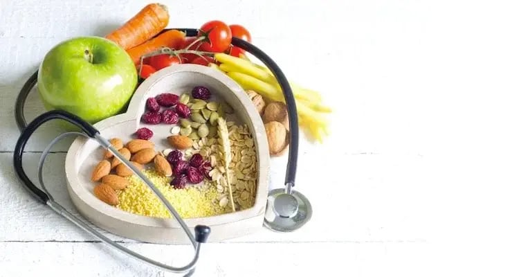 Alimentos saludables en recipiente con forma de corazón junto a un estetoscopio para cuidado del corazón