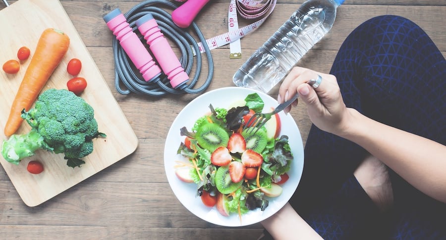 Plato con ensalada fresca, frutas, vegetales, botella de agua y accesorios de ejercicio que representan hábitos saludables y control del peso.