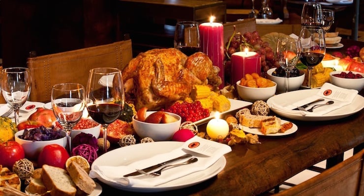 Mesa con cena navideña que incluye pavo, frutas, vino y velas encendidas
