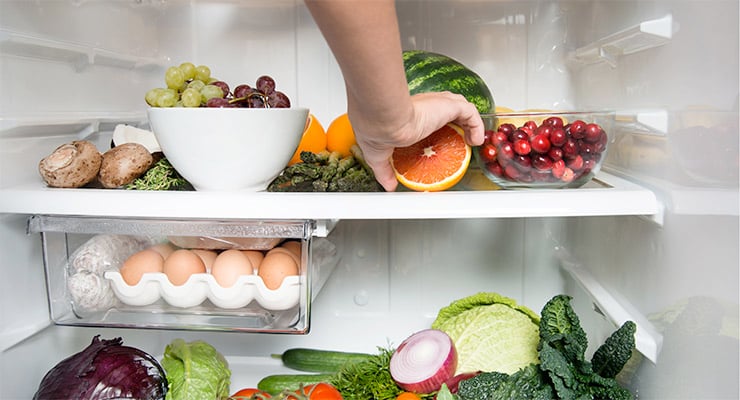 Persona tomando una naranja dentro de un refrigerador con alimentos frescos