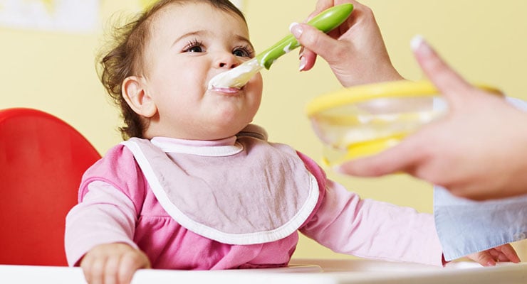 Bebé sentado en silla alta mientras un adulto le da comida con cuchara
