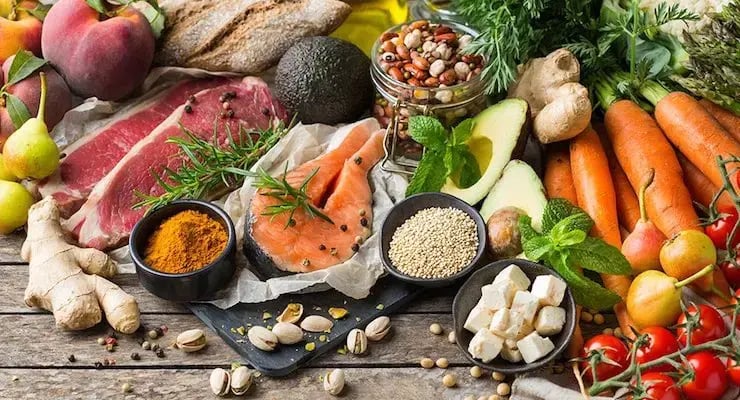 Variedad de alimentos frescos como vegetales, carnes, semillas y pescado sobre una mesa de madera.