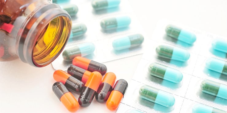 Cápsulas y blísteres de medicamentos junto a un frasco abierto sobre una superficie blanca