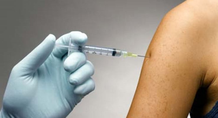 Mano con guante aplicando una vacuna con jeringa en el brazo de una persona