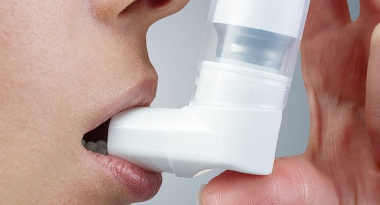 Persona usando inhalador para el tratamiento del asma mediante aplicación bucal.