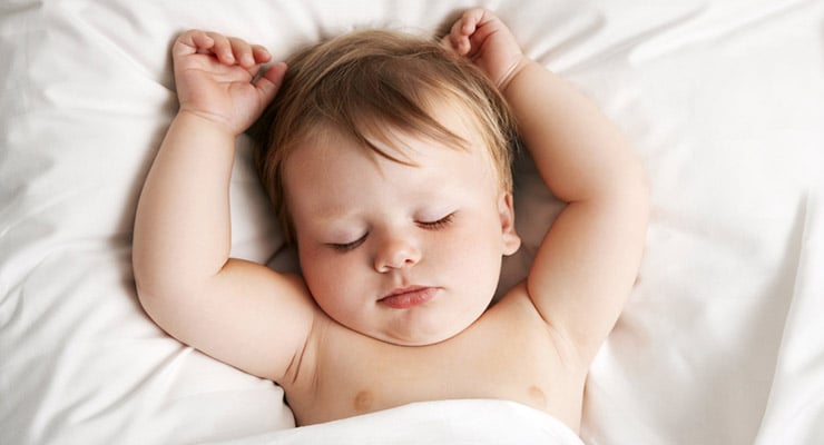 Bebé durmiendo boca arriba en una cama con sábanas blancas
