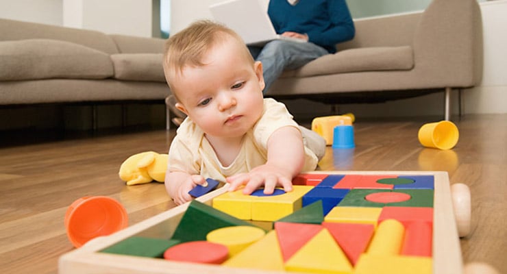 Bebé jugando con juguetes de estimulación temprana sobre el piso de la sala