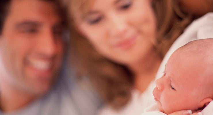 Bebé recién nacido en primer plano con dos adultos desenfocados al fondo