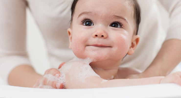 Bebé sonriente siendo bañado por un adulto con espuma en el agua