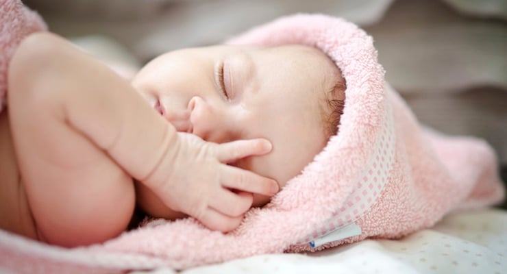 Bebé recién nacido durmiendo envuelto en una toalla rosada