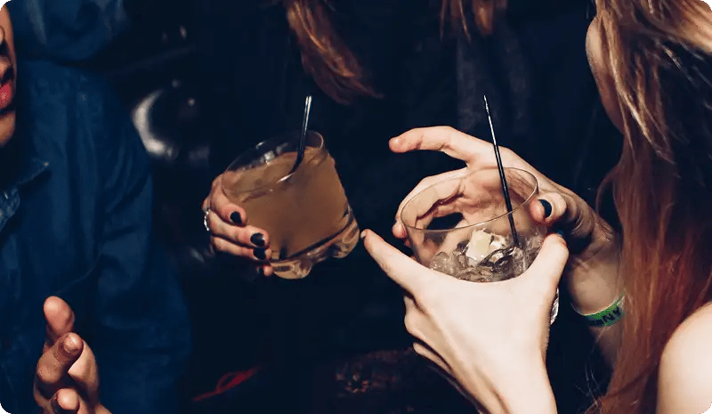 Personas sostienen bebidas con hielo mientras conversan en ambiente nocturno