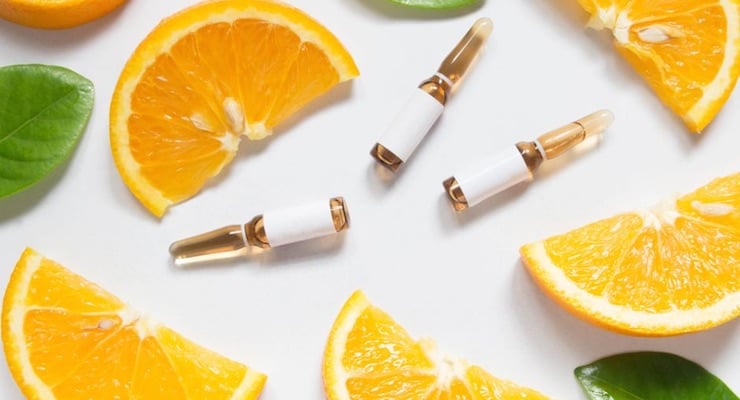 Rodajas de naranja y ampollas de vitamina C sobre fondo claro