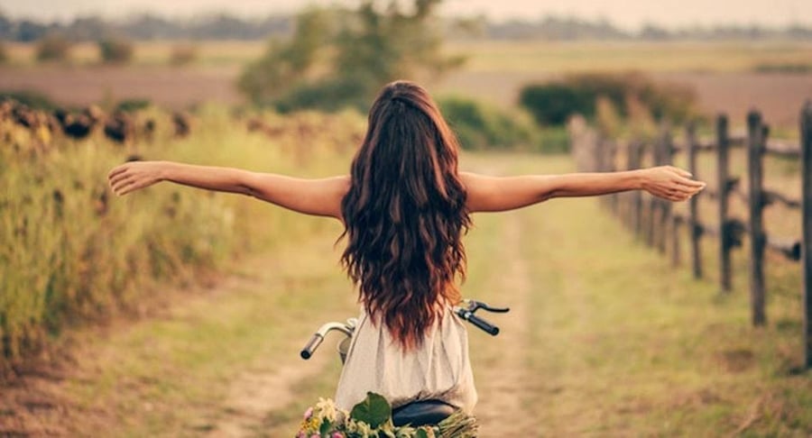 Persona sentada en bicicleta con los brazos extendidos en un camino rural rodeado de naturaleza.
