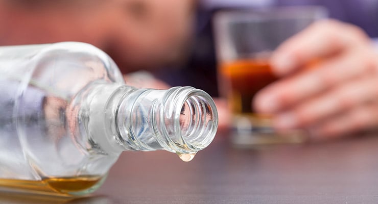 Botella de licor abierta sobre una mesa con una persona sosteniendo un vaso al fondo