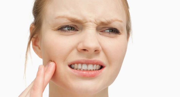 Mujer tocándose la mandíbula con gesto de dolor en la zona facial