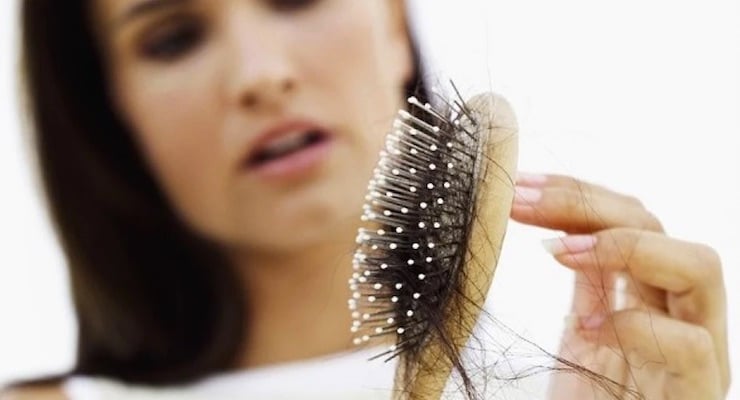 Mujer observando un cepillo con mechones de cabello acumulados