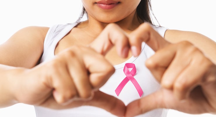 Mujer formando un corazón con las manos y un lazo rosado en el pecho, símbolo de concientización sobre el cáncer de mama.