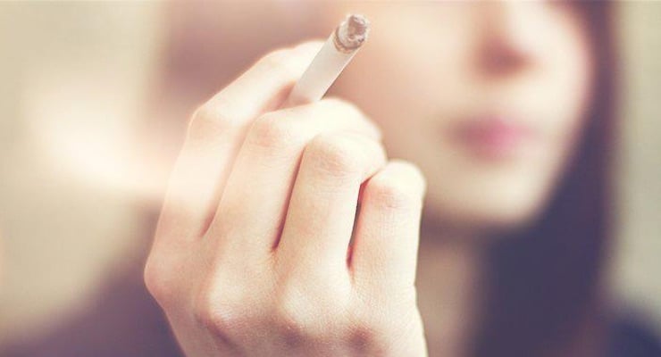 Mujer sosteniendo un cigarrillo encendido en primer plano con el rostro desenfocado al fondo
