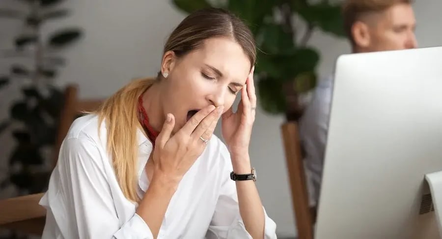 Mujer cansada en la oficina bostezando frente a la computadora por fatiga laboral