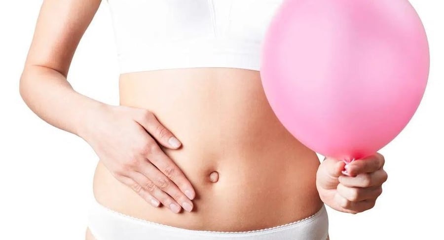 Primer plano del abdomen de una mujer sosteniendo un globo rosado inflado, simbolizando la sensación de hinchazón y distensión abdominal.