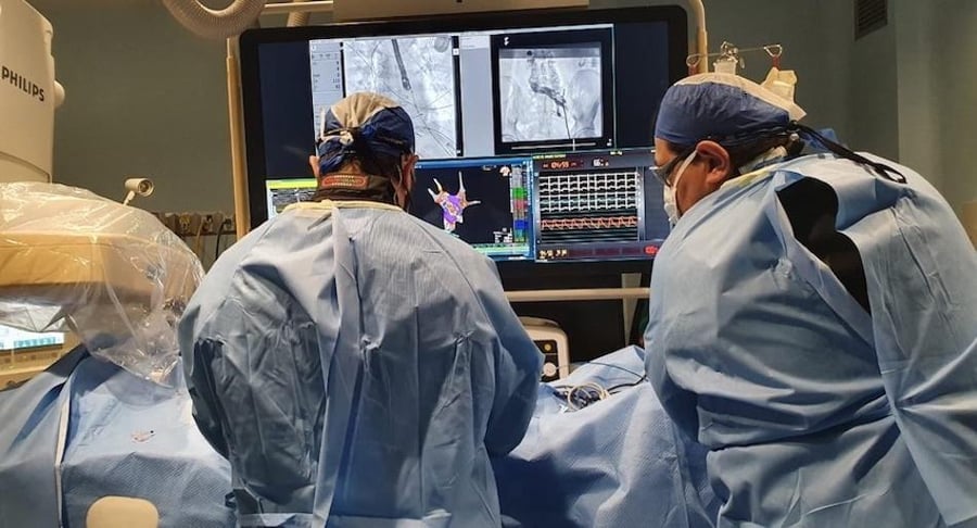 Especialistas del Hospital Clínica Bíblica de espaldas, realizando un procedimiento quirúrgico frente a múltiples monitores de alta tecnología que muestran imágenes cardiovasculares detalladas.