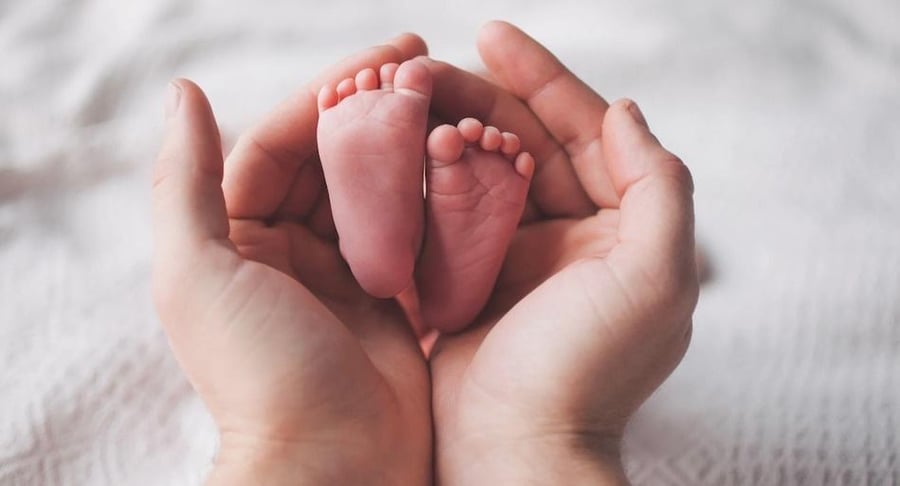 Manos de un adulto sosteniendo con delicadeza los pies de un bebé recién nacido en el Centro de Tamizaje.