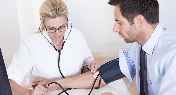 Médica midiendo la presión arterial de un paciente durante un chequeo médico en consultorio.