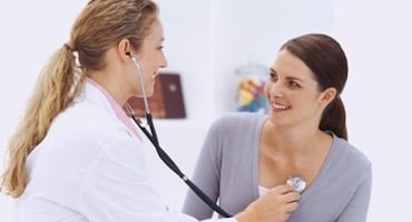 Doctora realizando una revisión médica con estetoscopio a una paciente sonriente, representando los planes de salud para mamá.