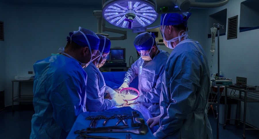 Equipo médico realiza una cirugía en un quirófano del Hospital Clínica Bíblica con iluminación quirúrgica y personal usando equipo de protección.