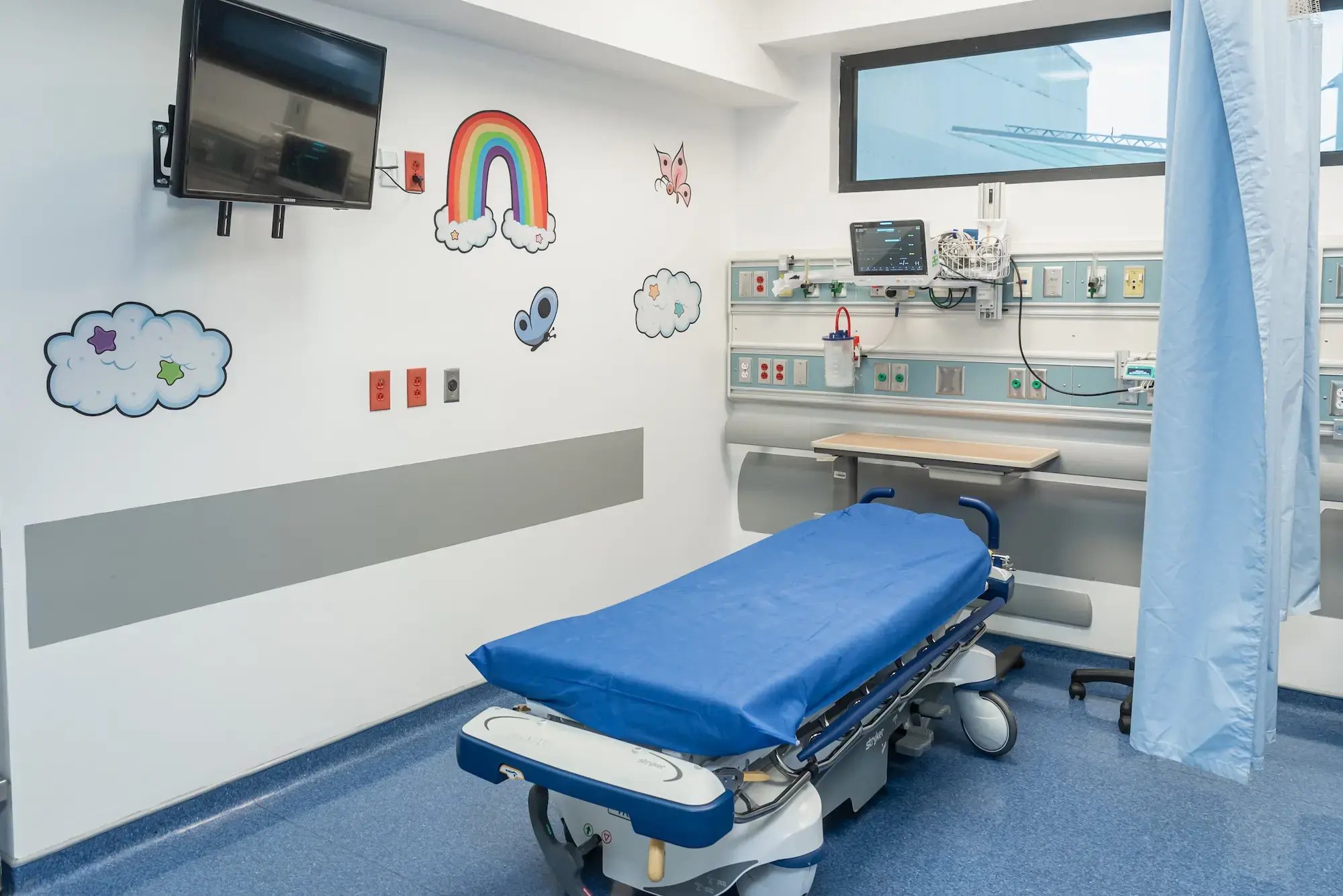 Cubículo de emergencias pediátricas en el Hospital Clínica Bíblica equipado con camilla, monitores médicos y decoración infantil en las paredes.