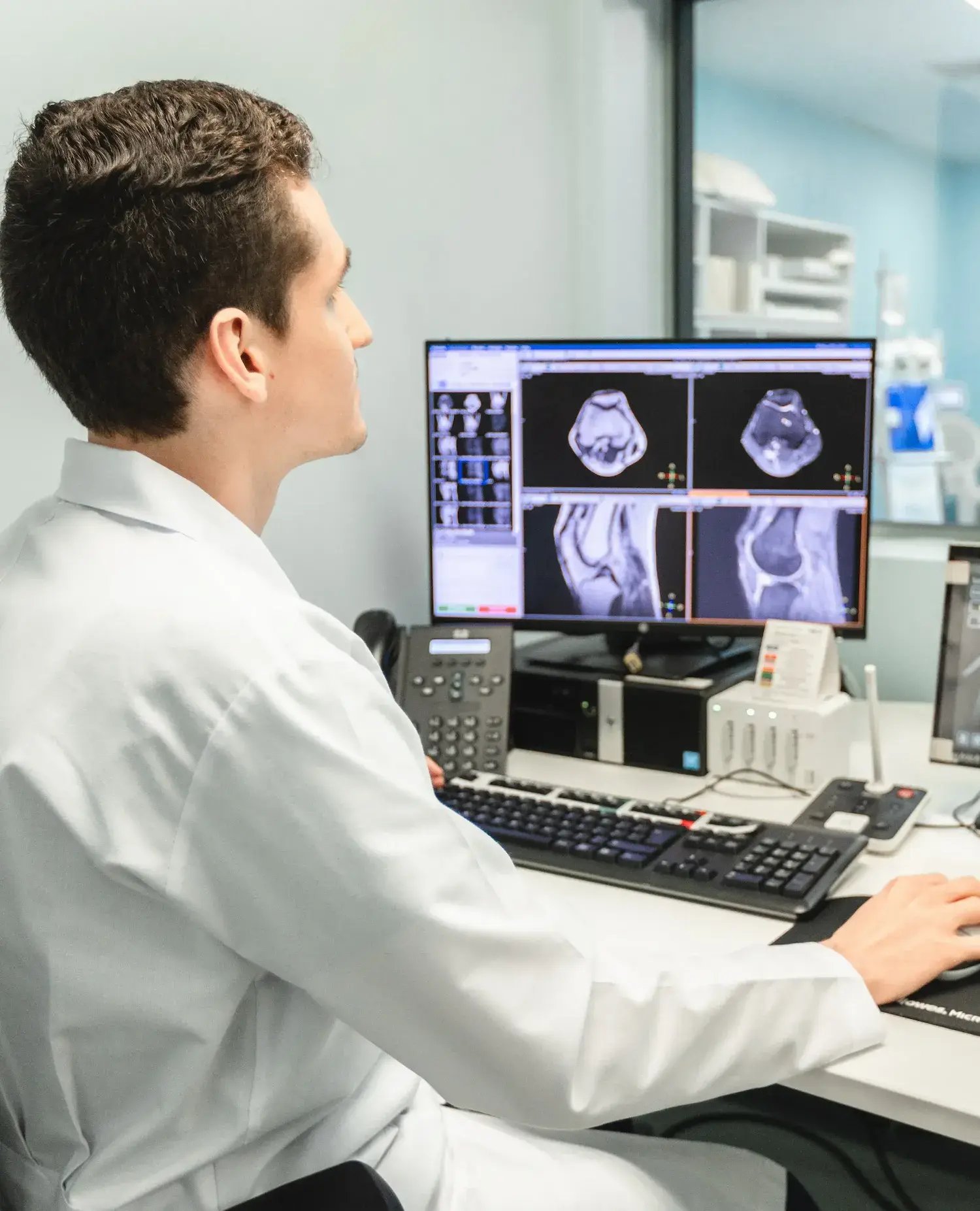 Radiologist at Hospital Clinica Biblica analyzing a knee MRI scan on high-resolution monitors from the diagnostic imaging control room.